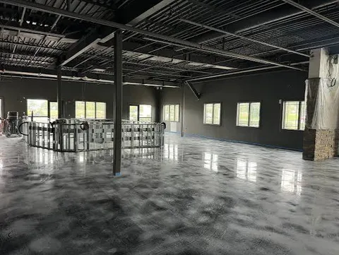 Open-plan commercial space under construction with exposed ceiling and a silver and charcoal metallic epoxy floor