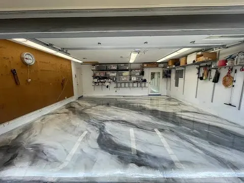 Two-car garage with pegboard and shelving and a white and gray marble metallic epoxy floor