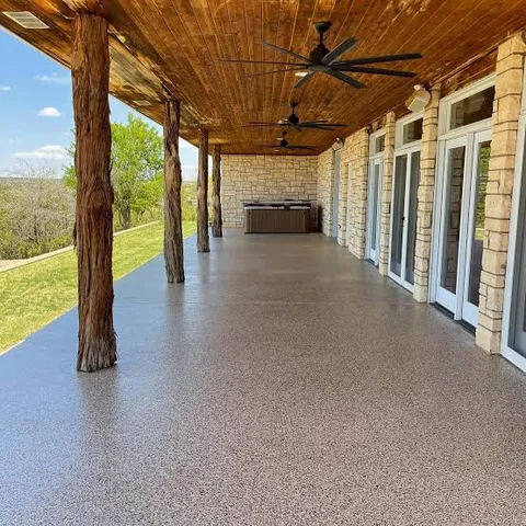 Long covered porch with cedar posts and a tan flake coated floor overlooking a lawn